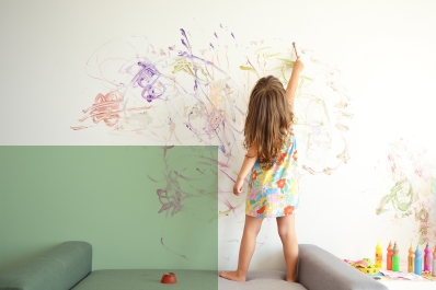 Picture of a little girl standing on the sofa and painting on the wall.